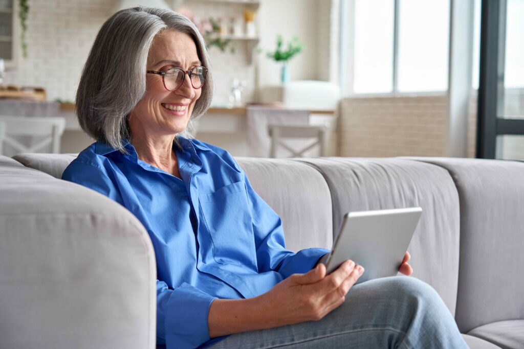 Ältere Frau macht auf dem Sofa Online-Therapie am Tablet in Praxis Dr. Jungclaussen, Düsseldorf in Deutschland